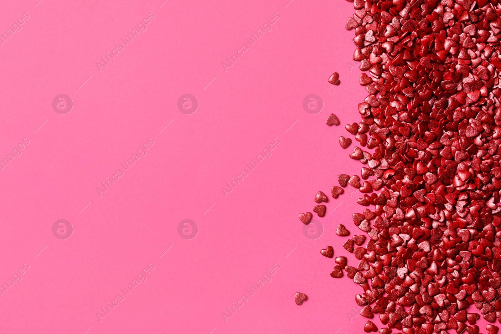 Photo of Red heart shaped sprinkles on pink background, flat lay. Space for text