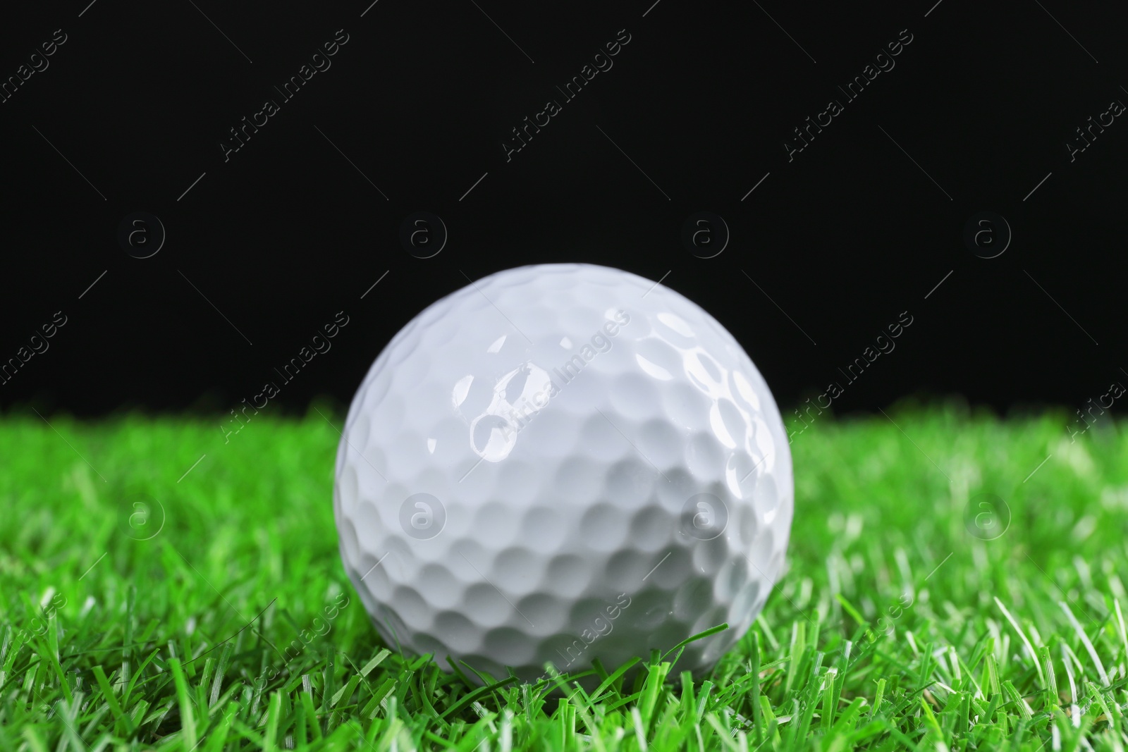 Photo of Golf ball on green grass against black background, closeup