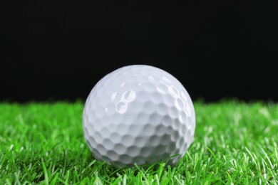 Photo of Golf ball on green grass against black background, closeup
