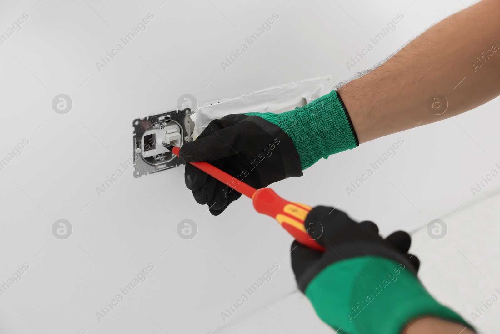 Photo of Electrician with screwdriver repairing power socket indoors, closeup