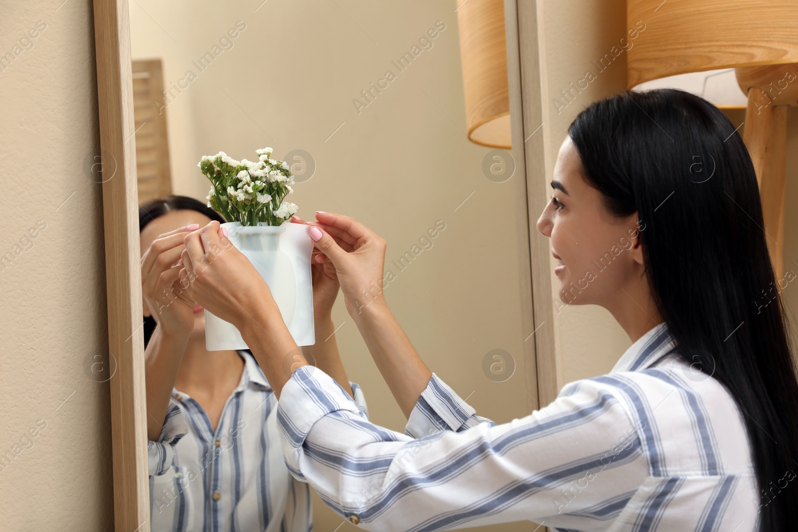 Photo of Woman attaching silicone vase with flowers to mirror in room