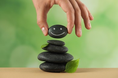 Photo of Woman putting stone with drawn happy face onto stack against blurred background, closeup. Zen concept