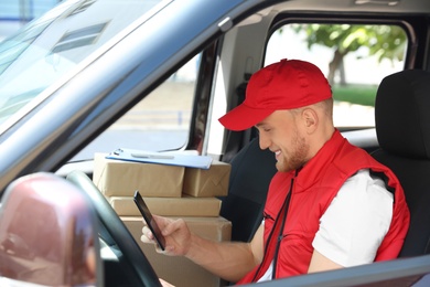 Young courier with smartphone and parcels in delivery car