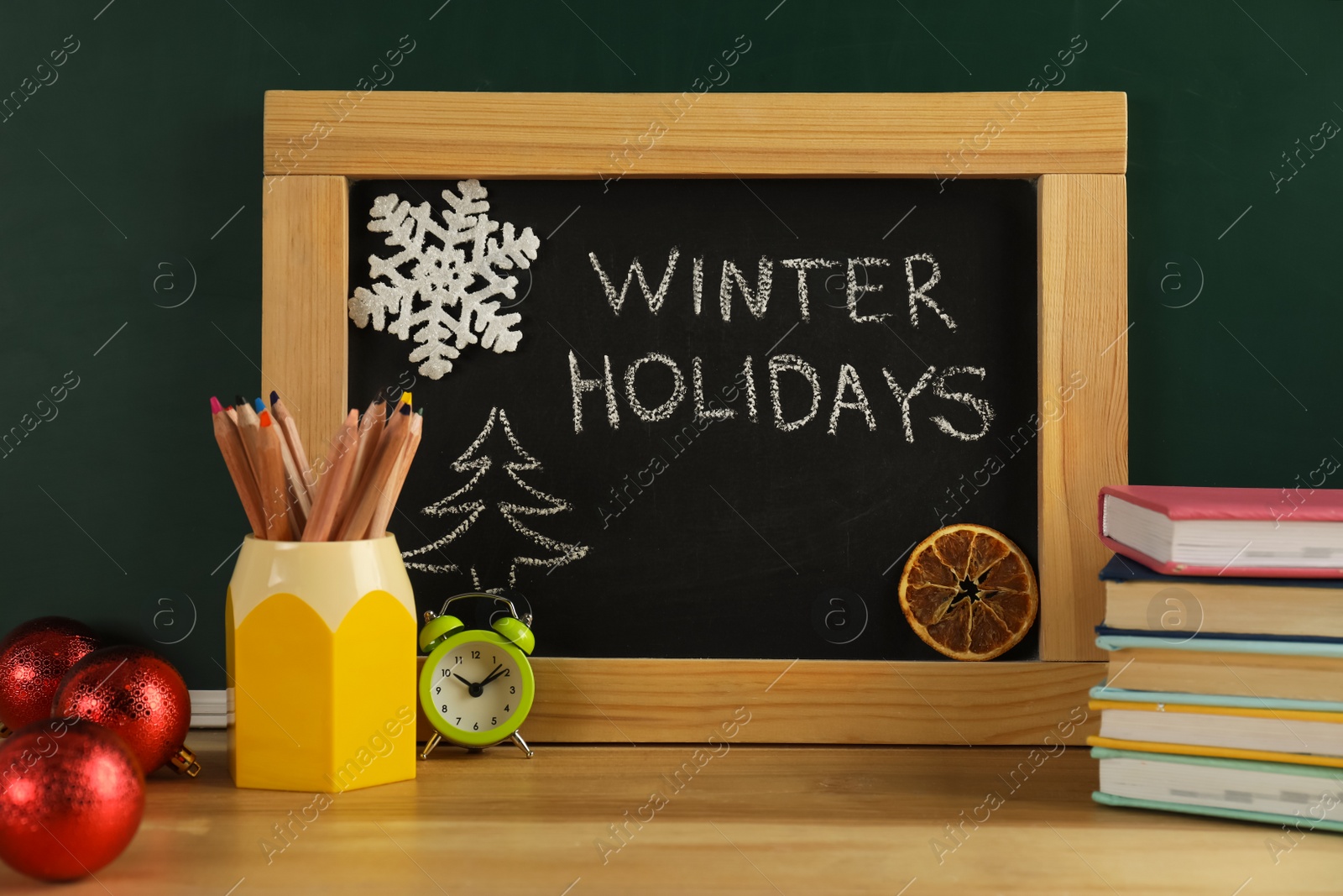 Photo of Chalkboard with text Winter Holidays, Christmas decor and school supplies on wooden table