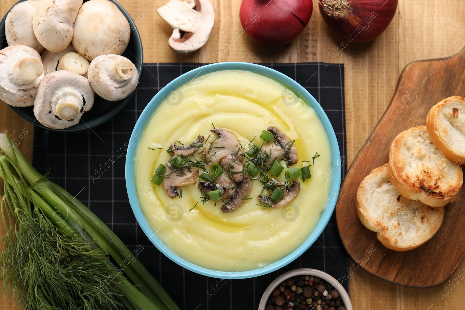 Photo of Bowl of tasty cream soup with mushrooms, green onions and dill on wooden table, flat lay