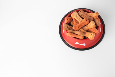 Photo of Bone shaped dog cookies in feeding bowl on white background, above view. Space for text