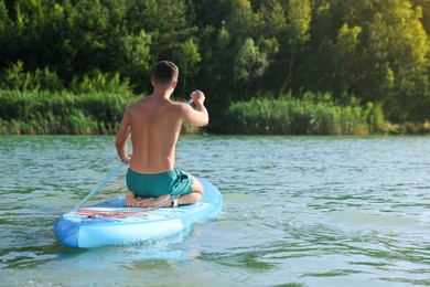 Photo of Man paddle boarding on SUP board in river, back view