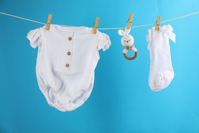 Baby clothes and accessories hanging on washing line against light blue background