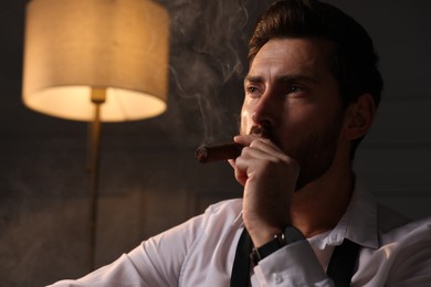 Handsome man smoking cigar at home. Space for text