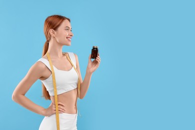 Photo of Happy young woman with bottle of pills and measuring tape on light blue background, space for text. Weight loss