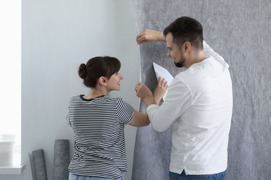 Photo of Woman and man hanging gray wallpaper in room