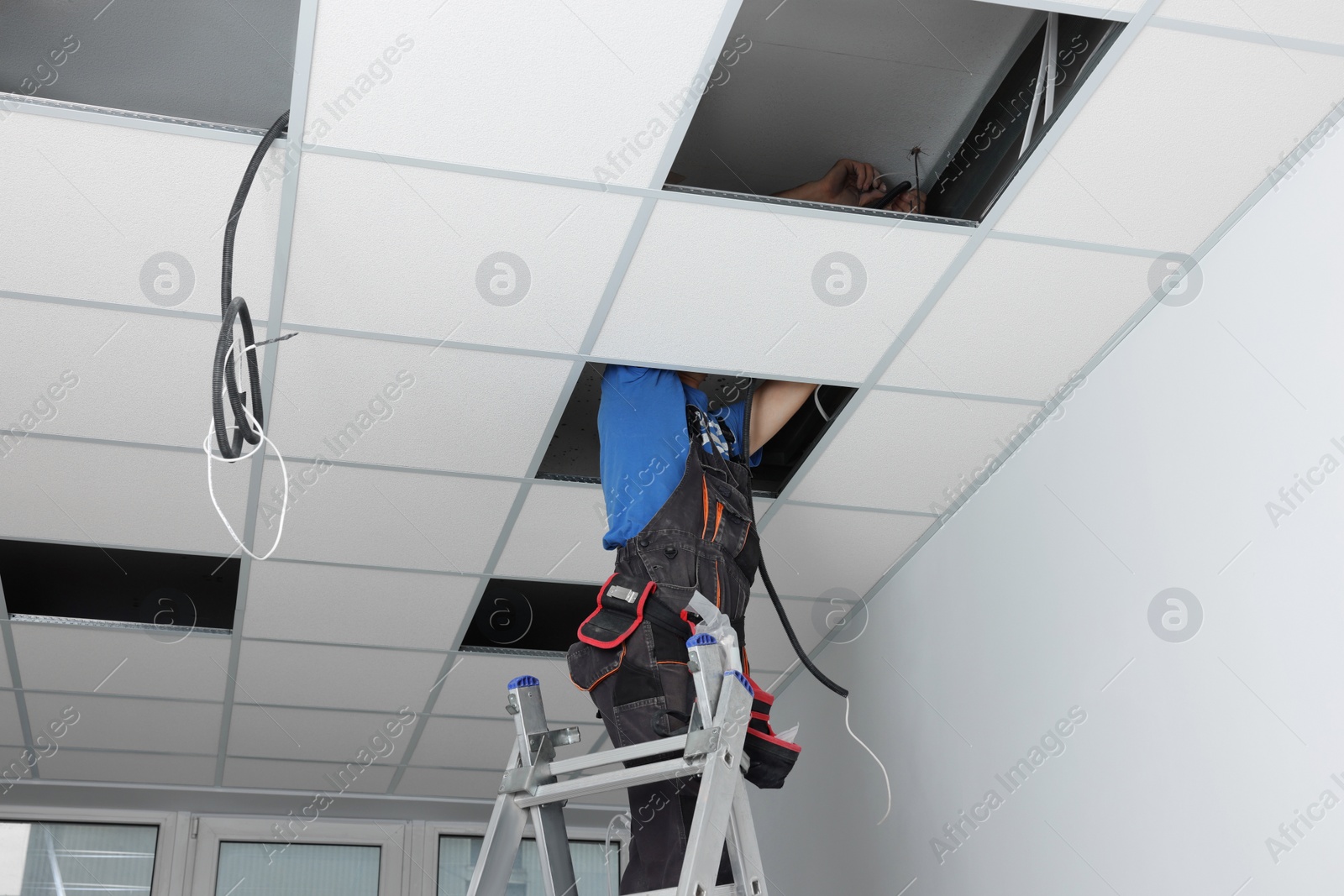 Photo of Installing ceiling lighting. Electrician working on step ladder in room