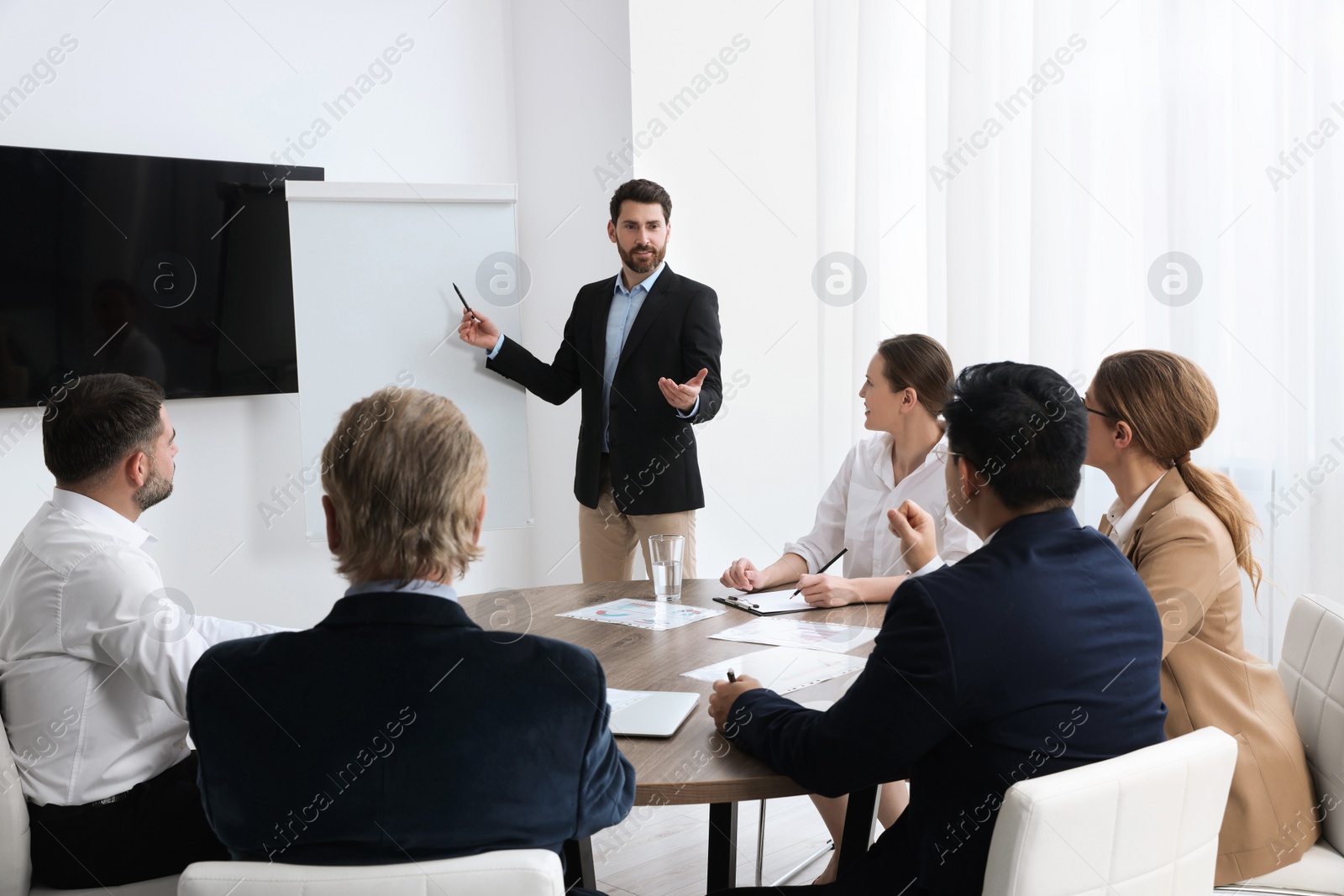 Photo of Business conference. Group of people listening to speaker report near tv screen in meeting room