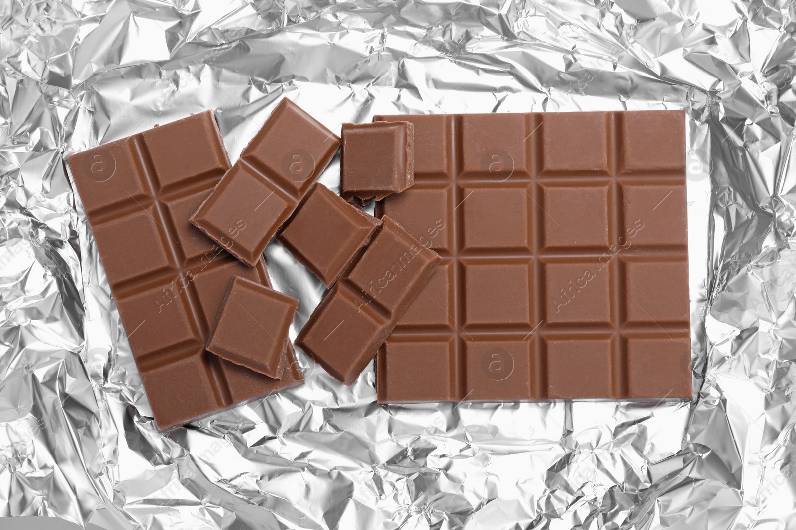 Photo of Pieces of delicious milk chocolate bars on foil, flat lay