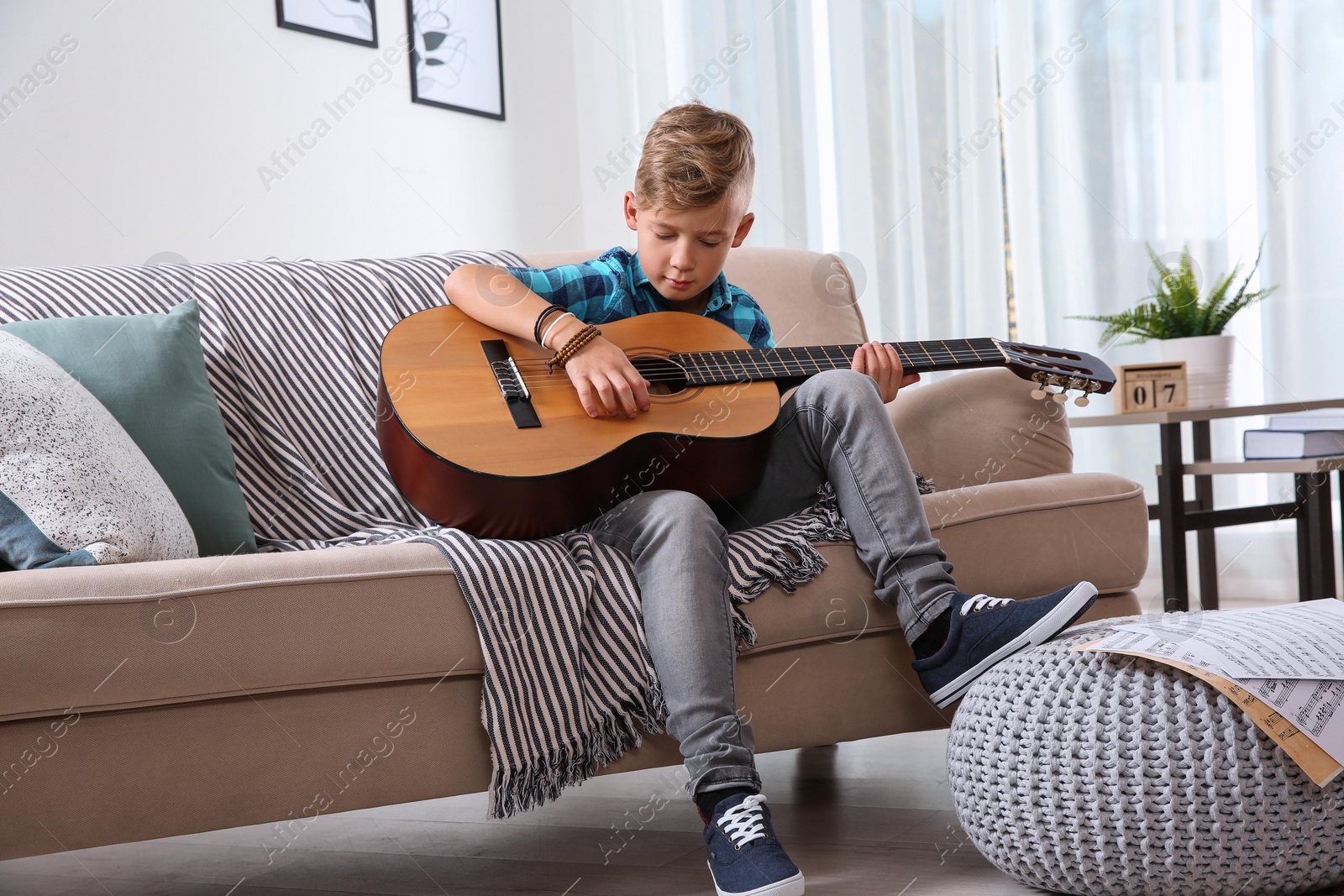 Photo of Cute little boy playing guitar on sofa in room