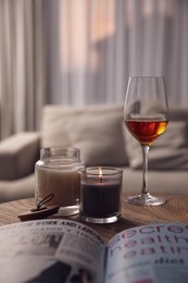 Photo of Glass of wine, burning candles and magazine on wooden table in living room