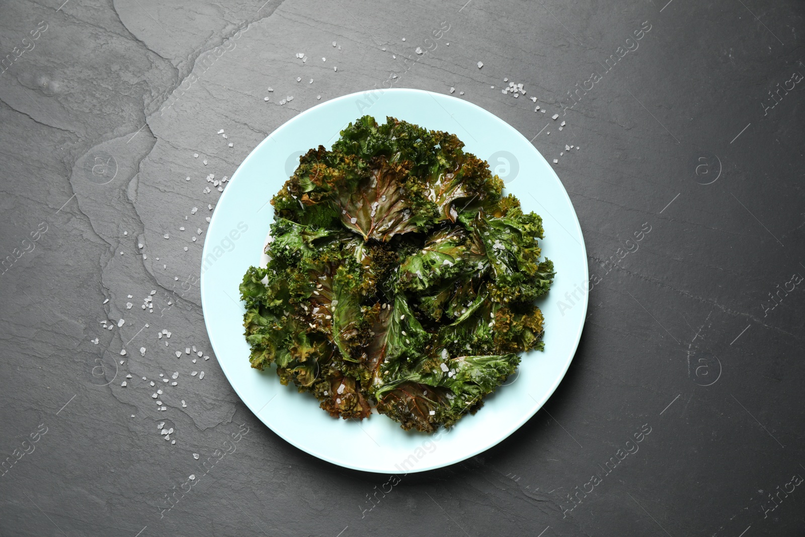 Photo of Tasty baked kale chips on dark grey table, top view