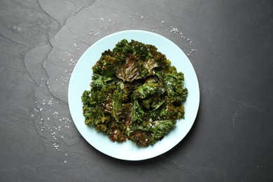 Tasty baked kale chips on dark grey table, top view