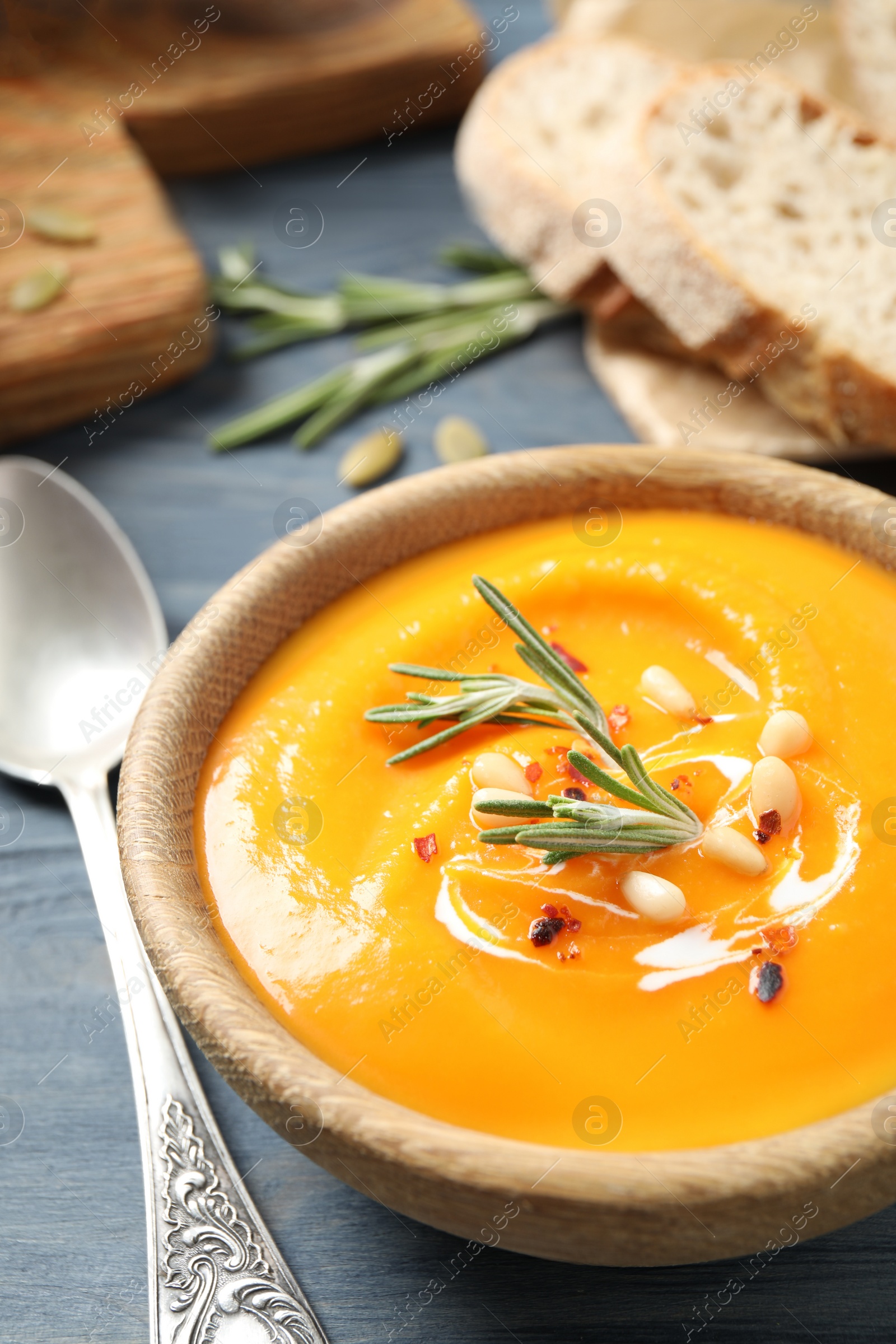 Photo of Delicious pumpkin soup in bowl on blue wooden table, closeup