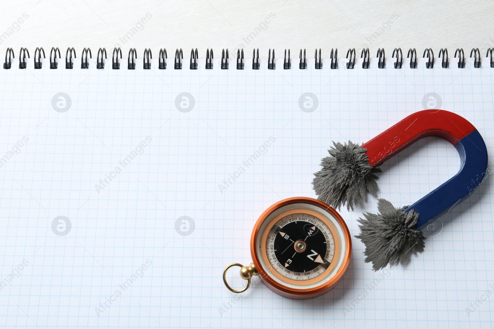 Photo of Compass and magnet with iron powder on notebook, top view. Space for text
