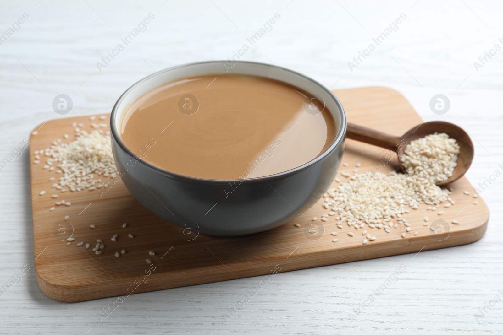 Photo of Tasty sesame paste and seeds on white wooden table