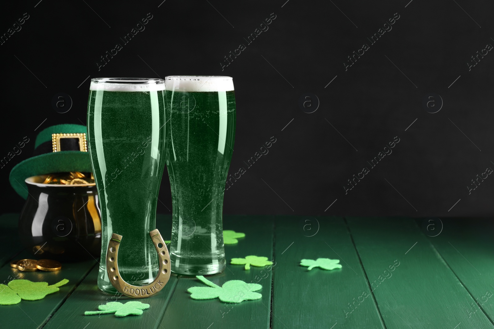 Photo of St. Patrick's day party. Green beer, leprechaun hat, pot of gold, horseshoe and decorative clover leaves on wooden table. Space for text