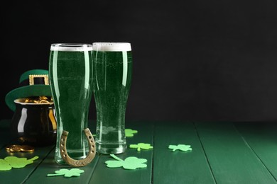 Photo of St. Patrick's day party. Green beer, leprechaun hat, pot of gold, horseshoe and decorative clover leaves on wooden table. Space for text