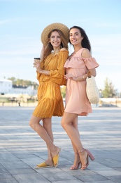 Beautiful young women in stylish dresses on city street