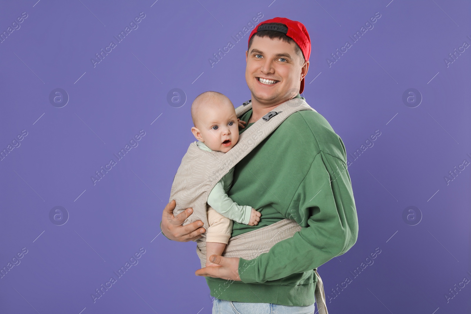 Photo of Father holding his child in sling (baby carrier) on purple background. Space for text