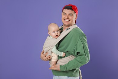 Father holding his child in sling (baby carrier) on purple background. Space for text