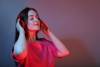 Portrait of beautiful woman with headphones on color background, space for text