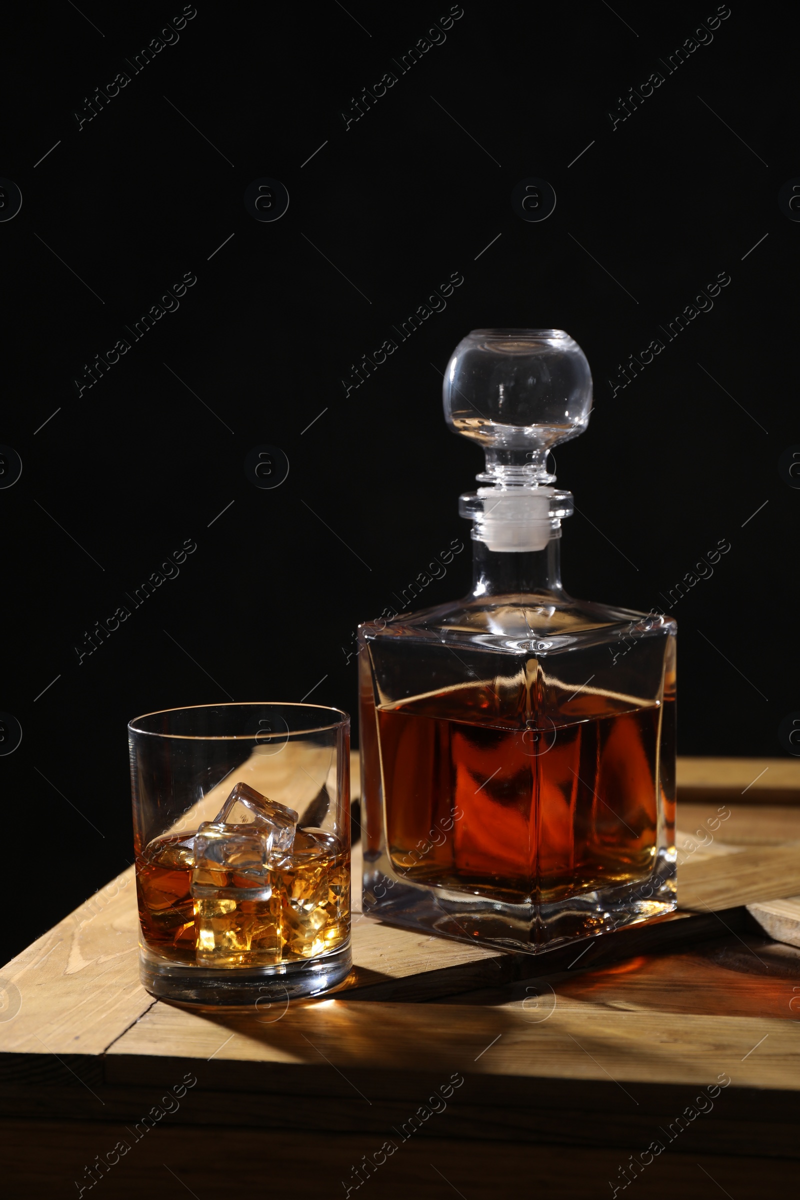 Photo of Whiskey with ice cubes in glass and bottle on wooden crate against black background