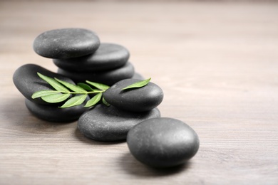 Photo of Black spa stones with branch on wooden background. Space for text