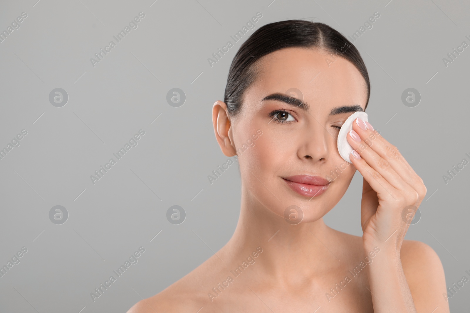 Photo of Beautiful woman removing makeup with cotton pad on light grey background. Space for text