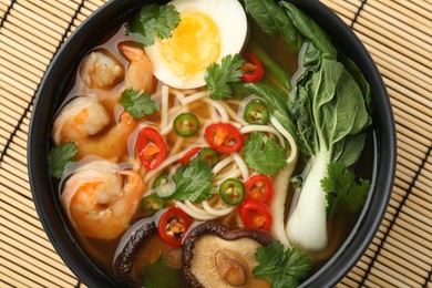 Delicious ramen with shrimps and egg in bowl on bamboo mat, top view. Noodle soup