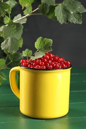 Ripe red currants and leaves in mug on green wooden table