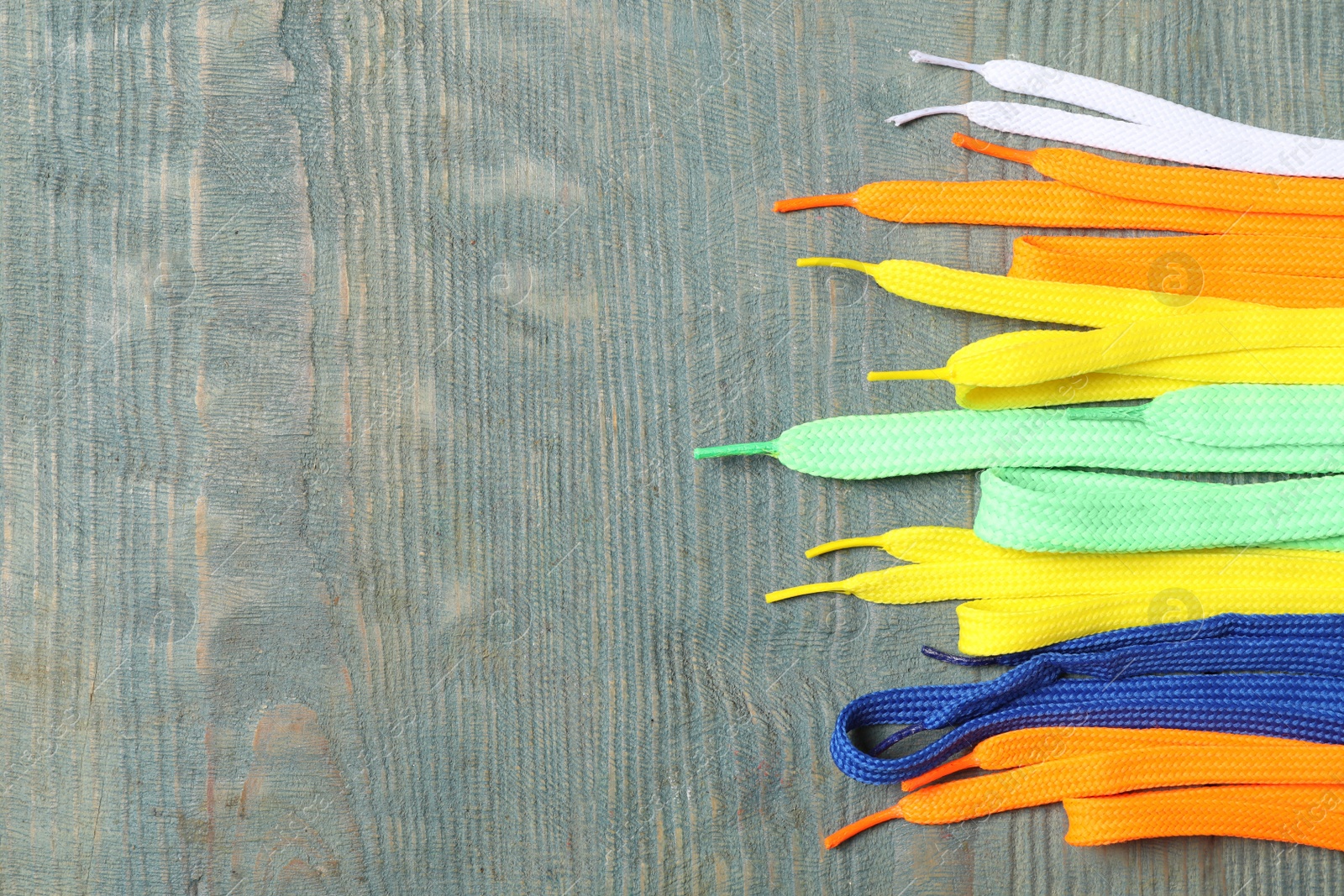 Photo of Colorful shoelaces on light blue wooden background, flat lay. Space for text