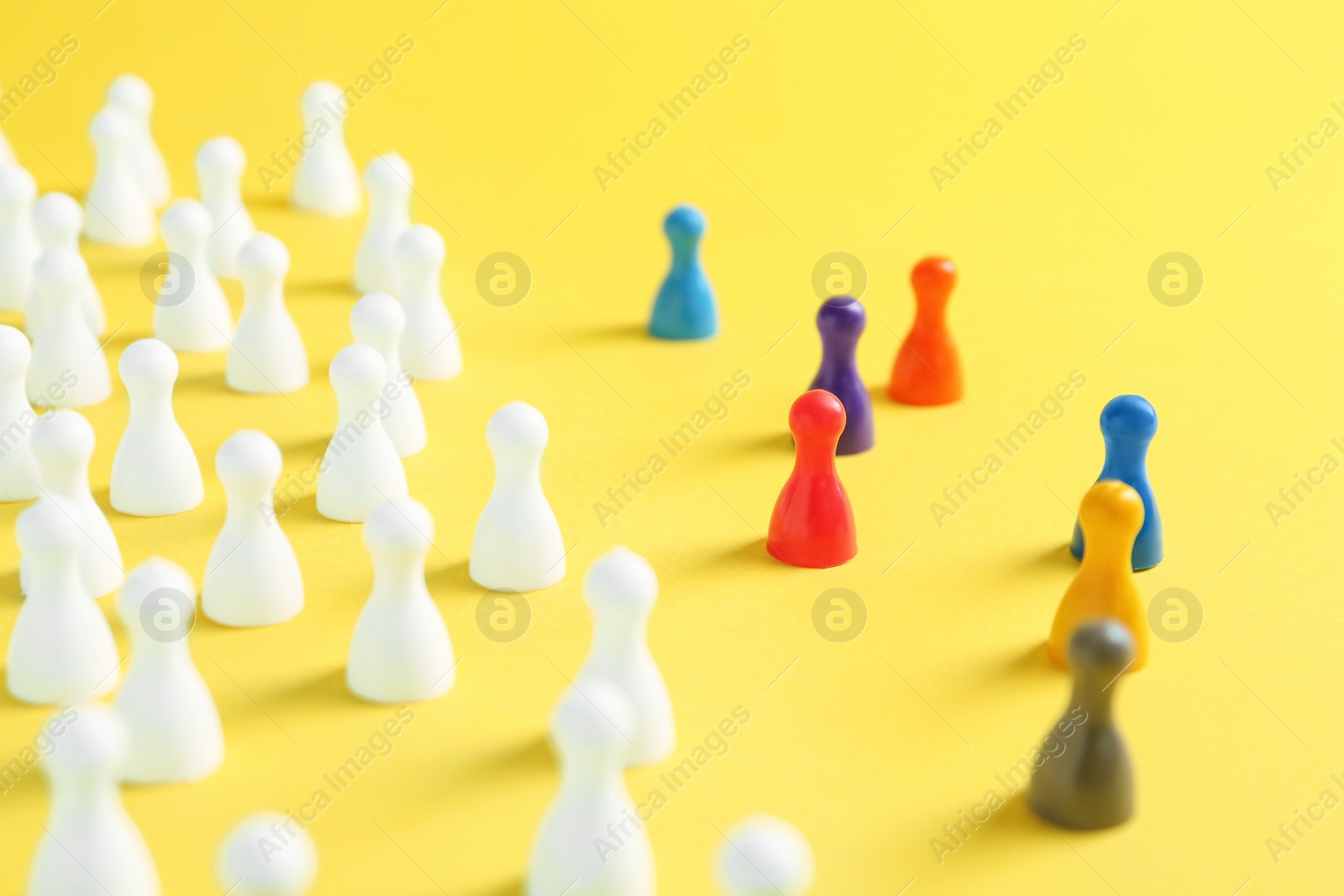 Photo of Colorful pawns on yellow background, closeup. Social inclusion concept