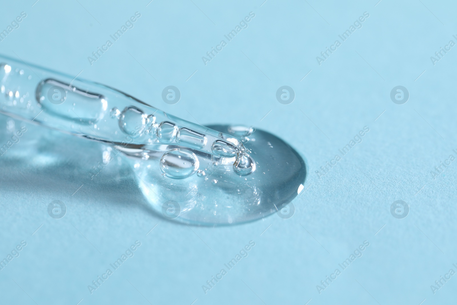 Photo of Glass pipette and transparent liquid on light blue background, closeup