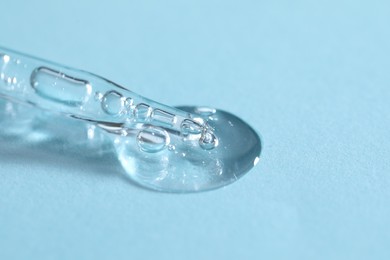 Glass pipette and transparent liquid on light blue background, closeup