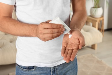 Man applying cream from tube onto hand at home, closeup