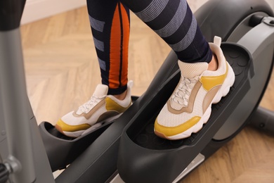 Photo of Woman using modern elliptical machine indoors, closeup