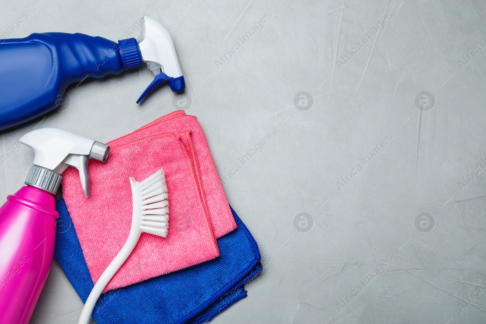 Photo of Microfiber cloths, brush and detergents on light grey table, flat lay. Space for text