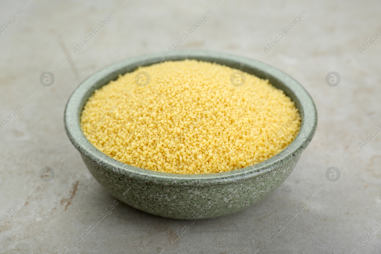 Photo of Bowl of raw couscous on light table, closeup