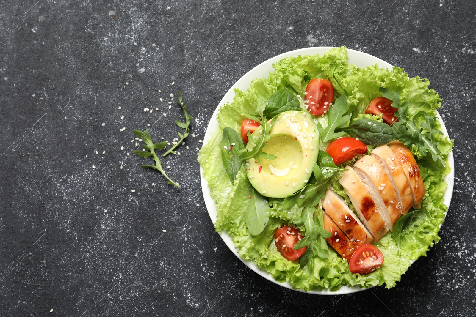 Photo of Delicious salad with chicken, cherry tomato and avocado on grey textured table, top view. Space for text