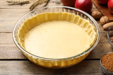 Raw dough and ingredients for apple pie on wooden table