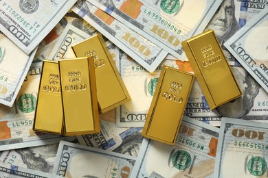 Photo of Many shiny gold bars on dollar banknotes, flat lay