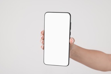 Woman holding smartphone with blank screen on light grey background, closeup. Space for text