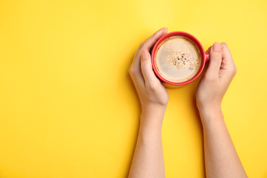 Woman with cup of coffee on yellow background, top view. Space for text