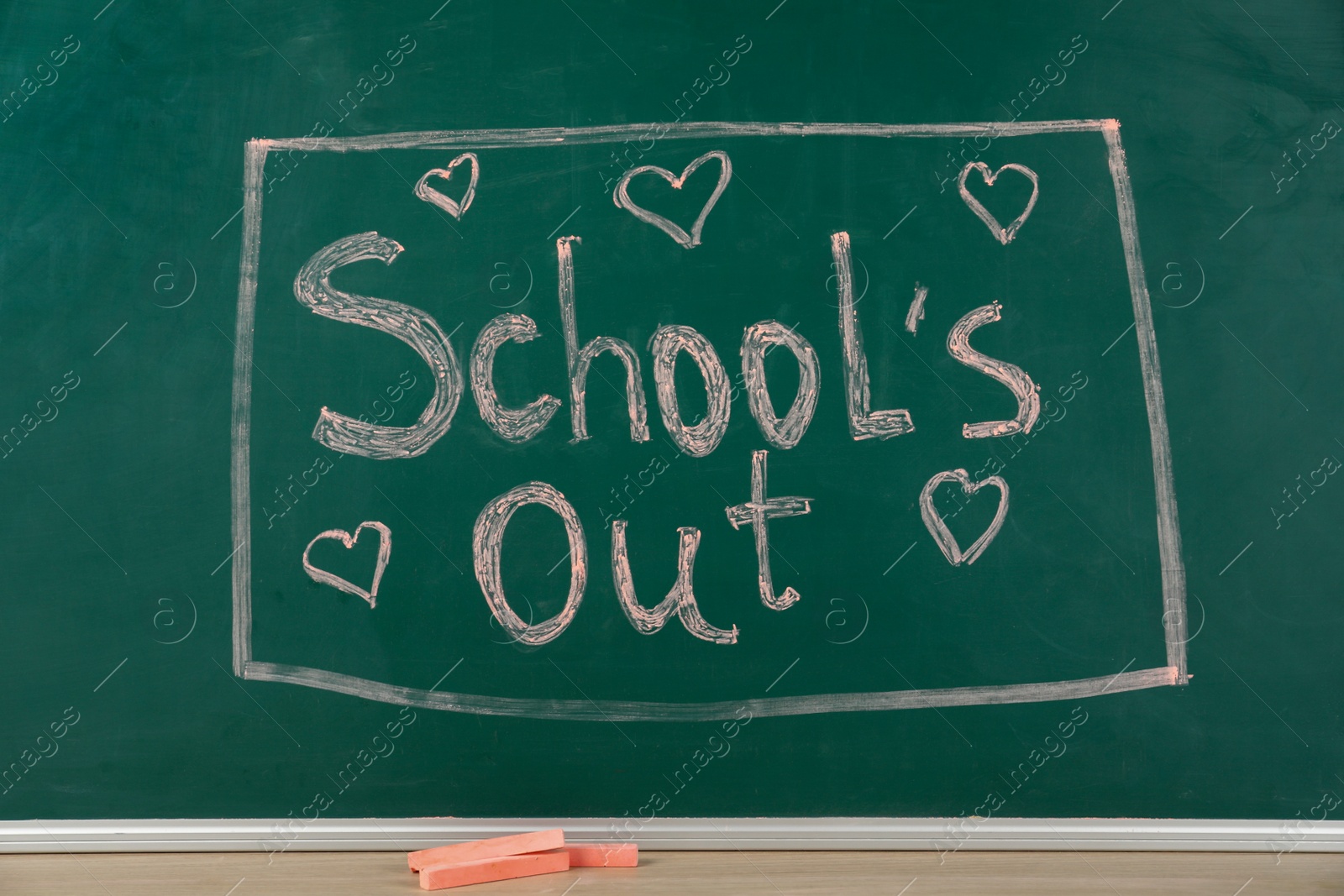 Photo of Pieces of color chalk on table near greenboard with text School's Out. Summer holidays